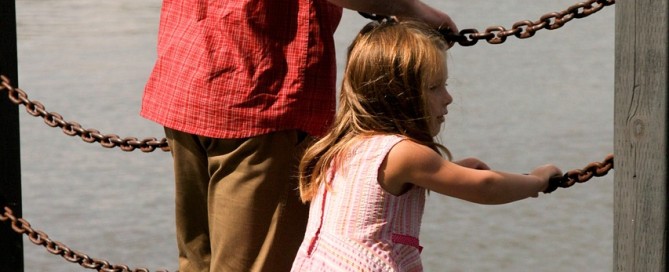 Picture of a man and young girl on a bridge looking at a lake.
