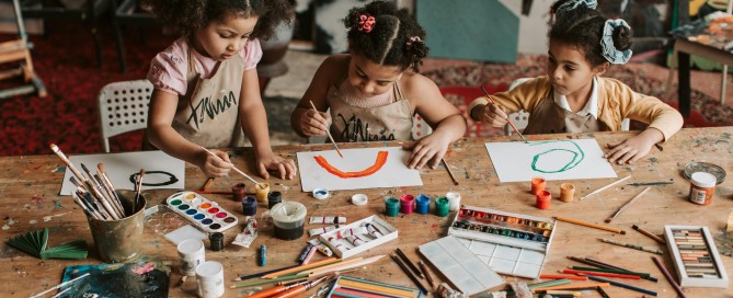 Three girls watercolor painting at a table.