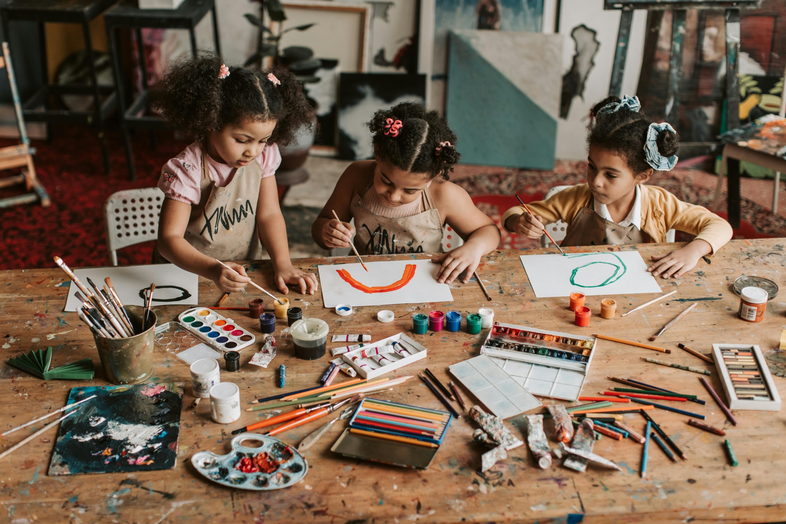 Three girls watercolor painting at a table.