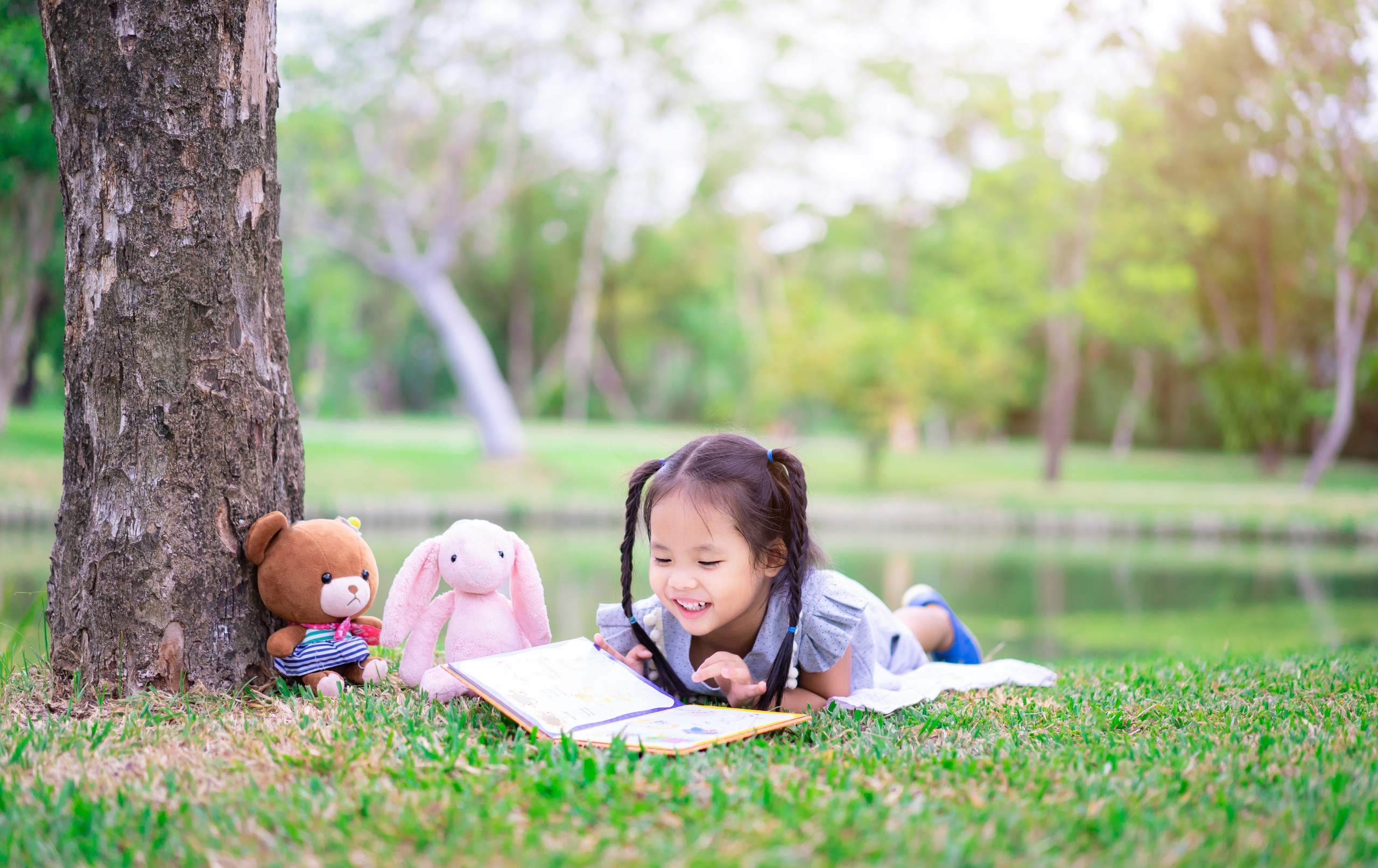 Photo of a girl reading a book outdoors laying on the grass.