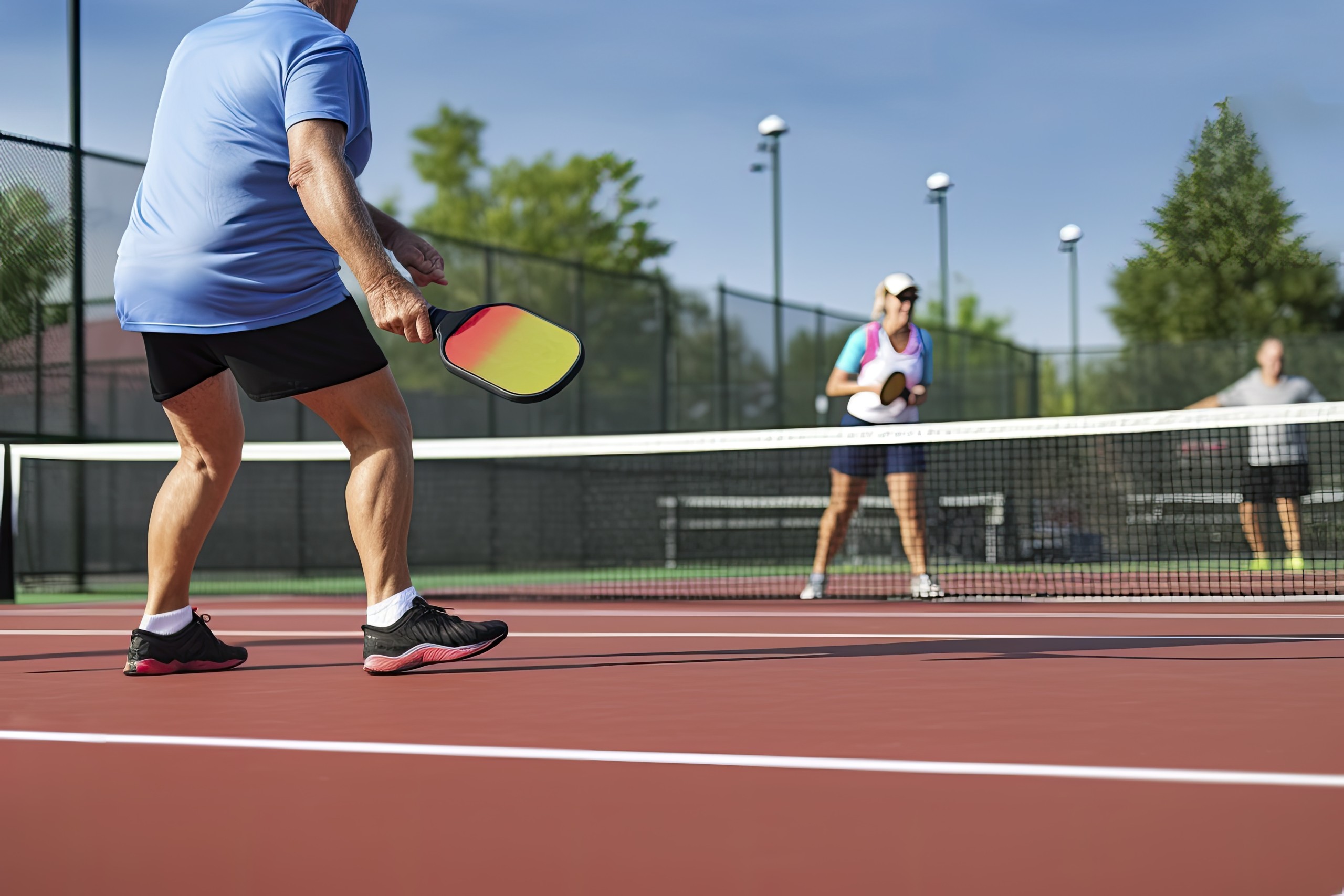 Picture of three adults playing pickleball at an outside court. Generative ai